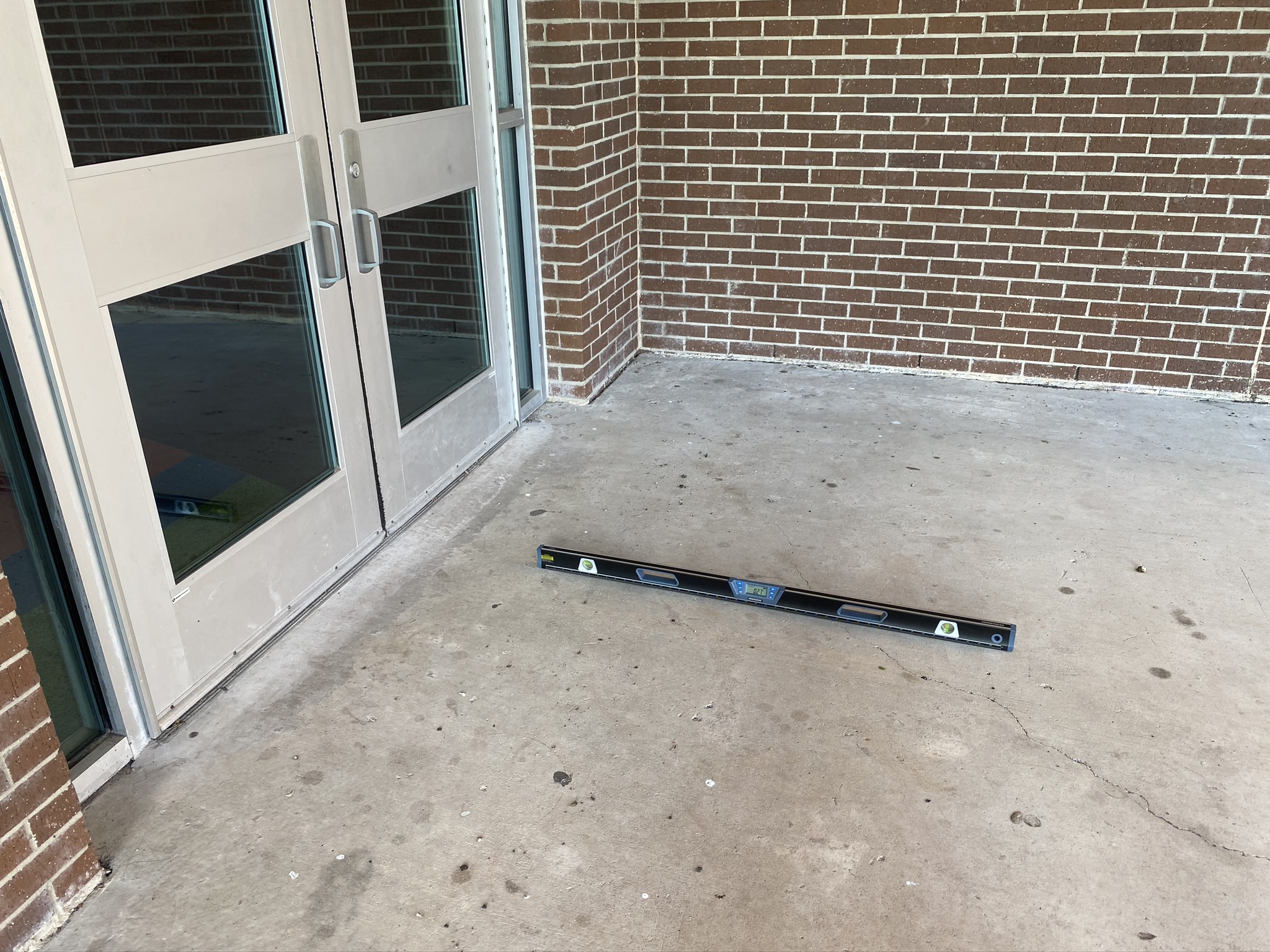 Picture of a door with concrete sidewalk and level to measure percent slope away from the door.