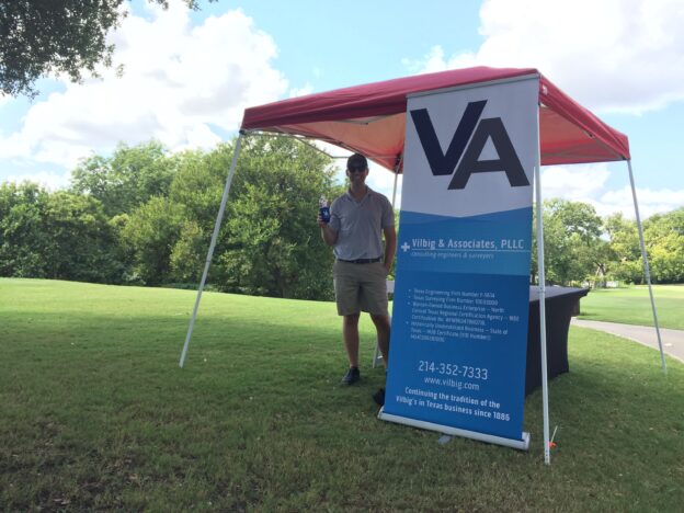 Tommy Vilbig next to a Vilbig & Associates banner under a tent on a golf course
